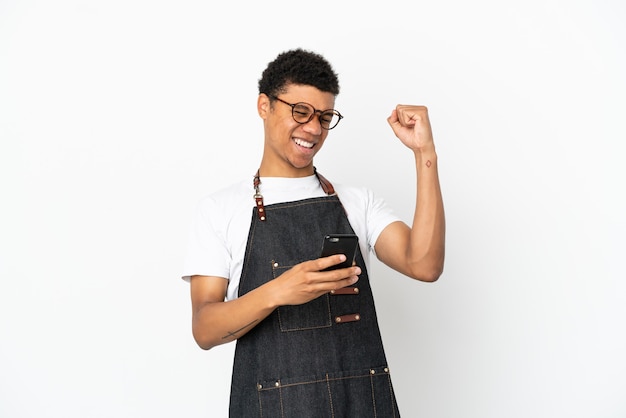 Restaurant Afro-Amerikaanse ober man geïsoleerd op een witte achtergrond met telefoon in overwinningspositie