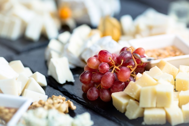 Restaurant cheese plate. Various types of cheeses with grape on black slate stone.