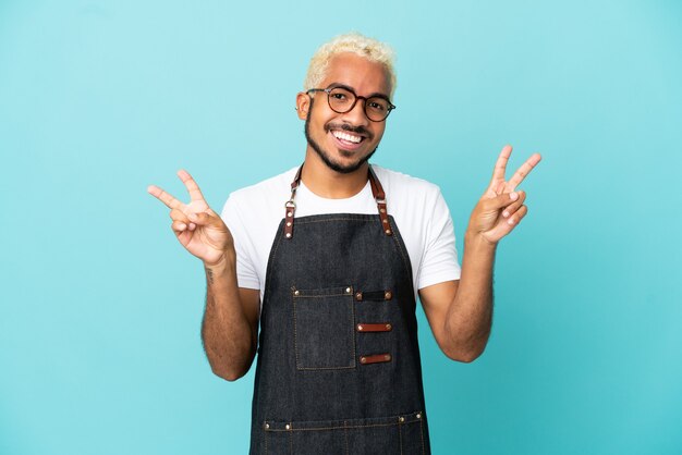 Restaurant Colombiaanse ober man geïsoleerd op blauwe achtergrond met overwinningsteken met beide handen