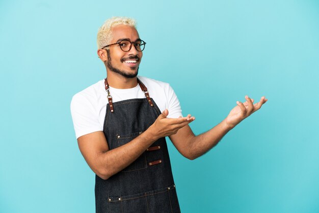 Restaurant Colombian waiter man isolated on blue background extending hands to the side for inviting to come