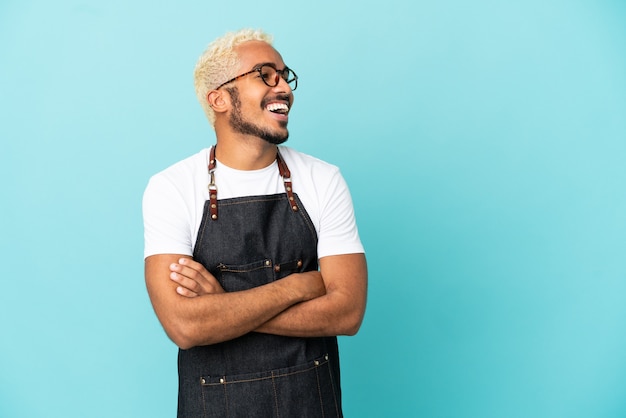 Restaurant Colombian waiter man isolated on blue background happy and smiling