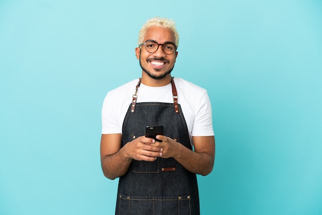 Restaurant Colombian waiter man isolated on blue background sending a message with the mobile