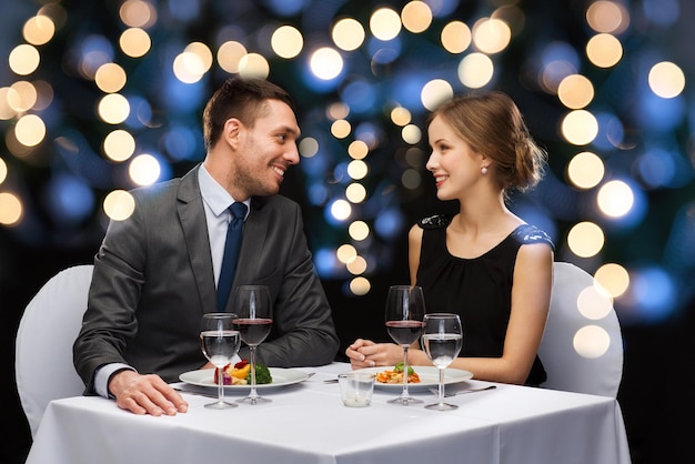 レストラン、カップル、休日のコンセプト-レストランで赤ワインとメインコースを食べる笑顔のカップル