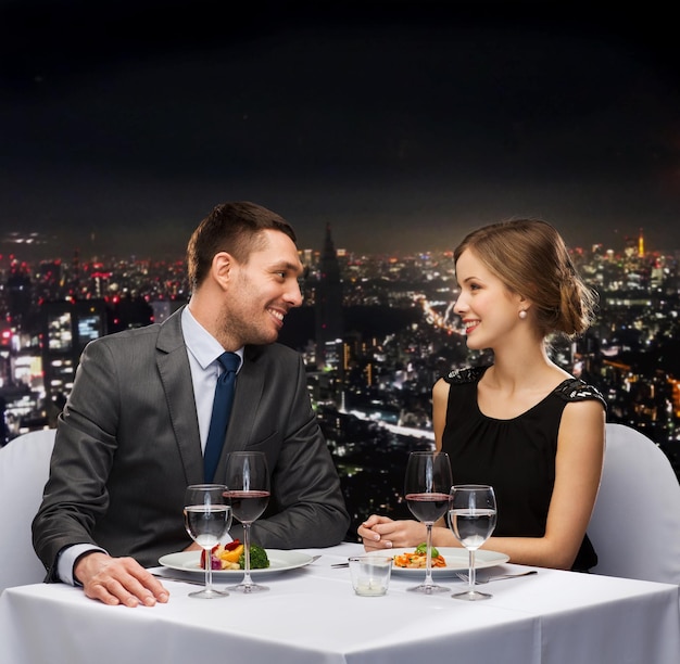 restaurant, couple and holiday concept - smiling couple eating main course with red wine at restaurant