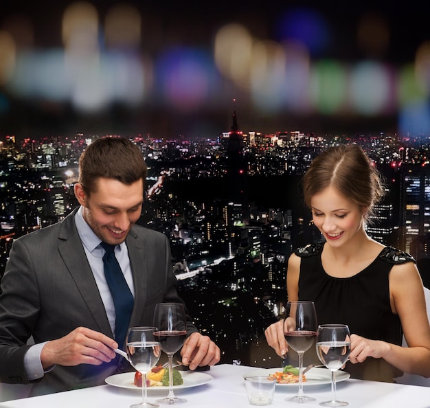 концепция ресторана, пары и праздника - улыбающаяся пара ест основное блюдо с красным вином в ресторане
