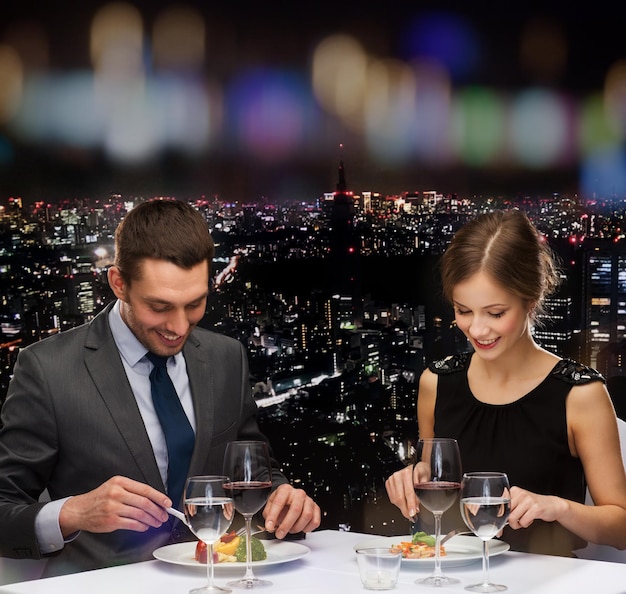 restaurant, couple and holiday concept - smiling couple eating main course with red wine at restaurant