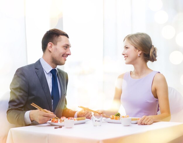 restaurant, couple and holiday concept - smiling couple eating sushi at restaurant