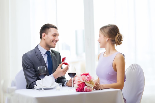 restaurant, couple and holiday concept - smiling man proposing to his girlfriend at restaurant