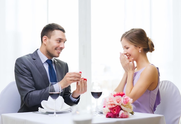 restaurant, couple and holiday concept - smiling man proposing to his girlfriend at restaurant