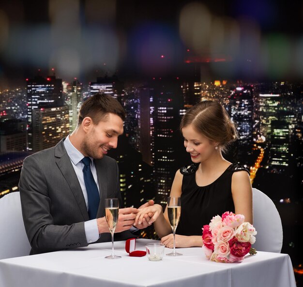 restaurant, couple and holiday concept - smiling man putting on finger engagement ring at restaurant