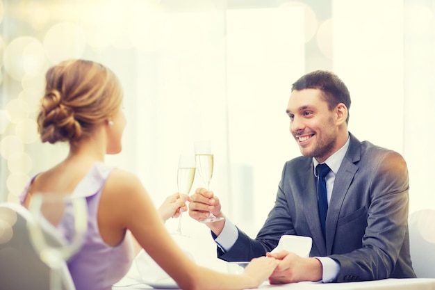 restaurant, couple and holiday concept - smiling man with glass of champagne looking at wife or girlfriend at restaurant