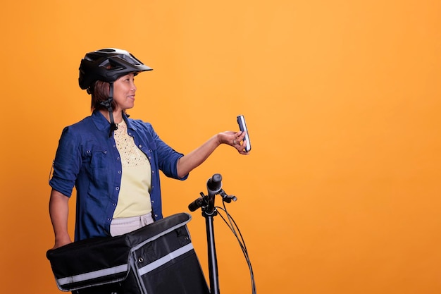 Restaurant employee with blue uniform and helmet delivering\
fast food order giving pos terminal to customer. pizzeria employee\
using bike as transportation while carrying takeout food\
backpack