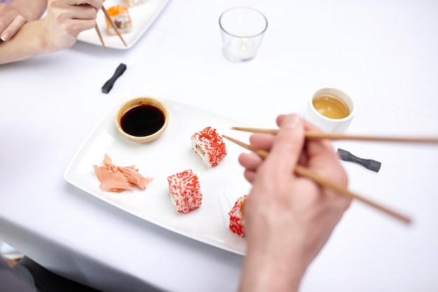 restaurant, food, people, date and holiday concept - close up of couple eating sushi at restaurant