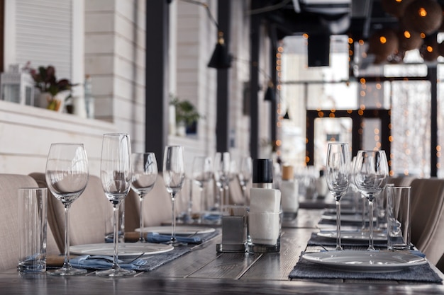 ヴィンテージグレーの木製テーブルの上の行に立つレストランのインテリア、サービングワインと水のグラス、プレート、フォーク、ナイフ、テキスタイルナプキンに