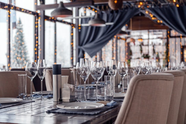 Restaurant interior, serving wine and water glasses, plates, forks and knives on textile napkins stand in a row on vintage gray wooden table