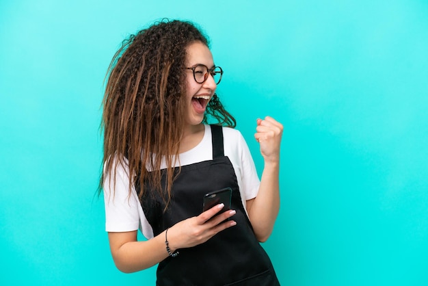 Restaurant ober Arabische vrouw geïsoleerd op blauwe achtergrond met telefoon in overwinningspositie