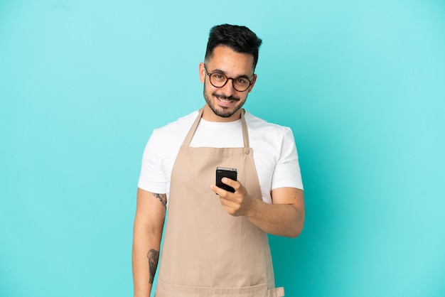 Restaurant ober blanke man geïsoleerd op blauwe achtergrond die een bericht verzendt met de mobiel