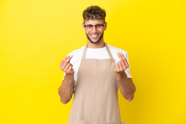 Restaurant ober blonde man geïsoleerd op gele achtergrond geld gebaar maken