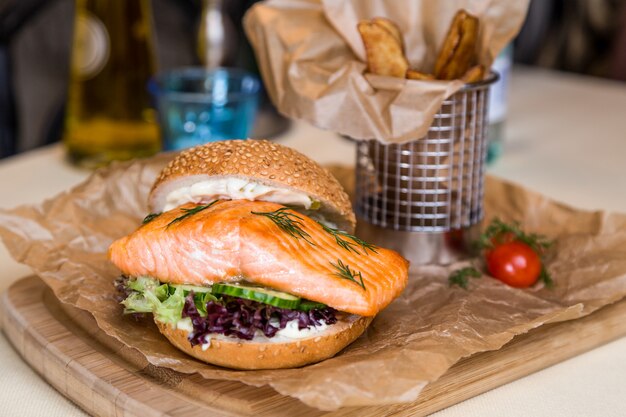 Restaurant serving dish - burger with salmon, frying potato on wooden board