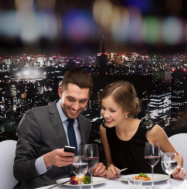 restaurant, technologie, paar en vakantieconcept - glimlachend paar dat een foto neemt van het hoofdgerecht met smartphonecamera in restaurant