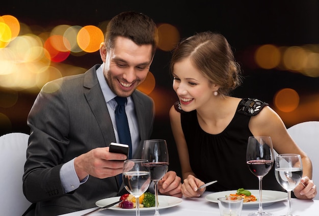 restaurant, technology, couple and holiday concept - smiling couple taking picture of main course with smartphone camera at restaurant