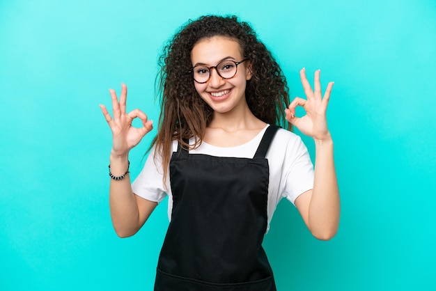 Restaurant waiter Arab woman isolated on blue background showing an ok sign with fingers