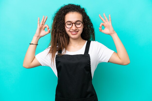 Restaurant waiter Arab woman isolated on blue background in zen pose