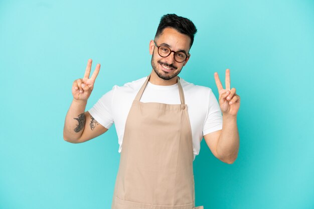 Restaurant waiter caucasian man isolated on blue background showing victory sign with both hands