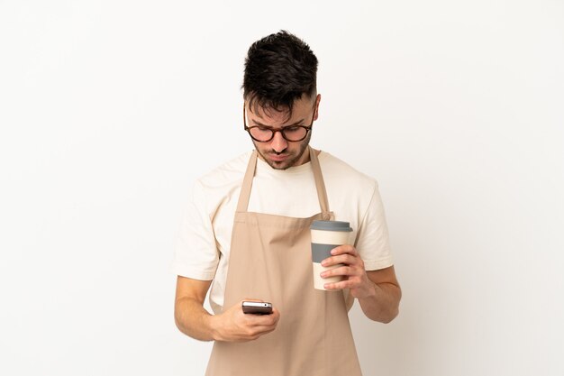 Restaurant waiter caucasian man isolated on white background holding coffee to take away and a mobile