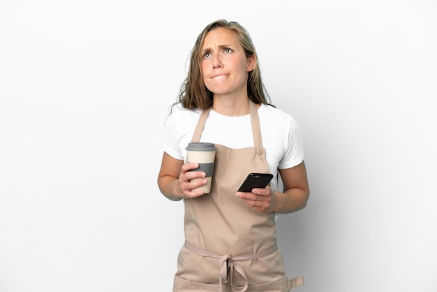 Restaurant waiter caucasian woman isolated on white background holding coffee to take away and a mobile while thinking something