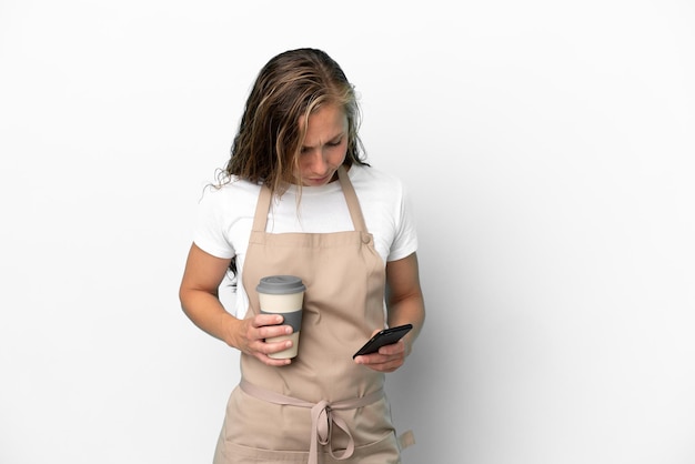 Foto donna caucasica del cameriere del ristorante isolata su fondo bianco che tiene il caffè da portare via e un cellulare