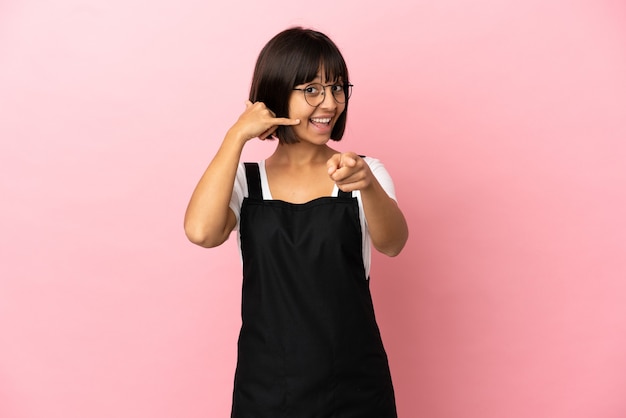 Restaurant waiter over isolated pink background making phone gesture and pointing front