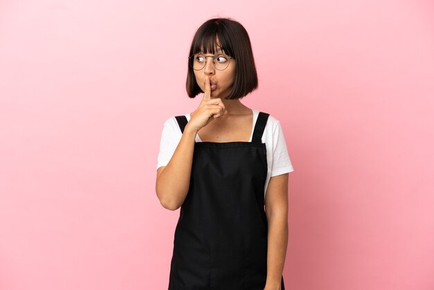 Restaurant waiter over isolated pink background showing a sign of silence gesture putting finger in mouth