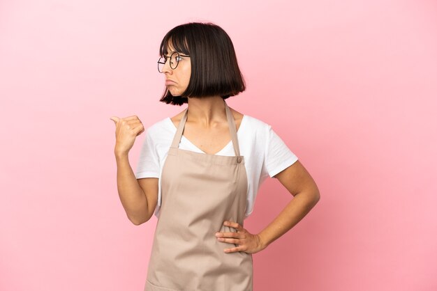 Restaurant waiter over isolated pink background unhappy and pointing to the side