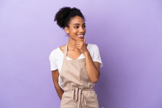 Restaurant waiter latin woman isolated on purple background looking to the side and smiling