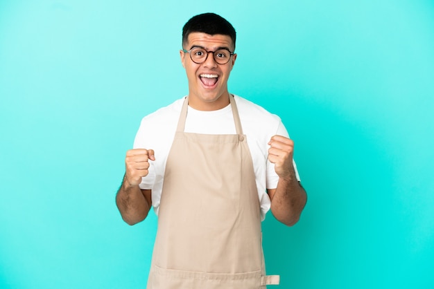 Restaurant waiter man over isolated blue background celebrating a victory in winner position