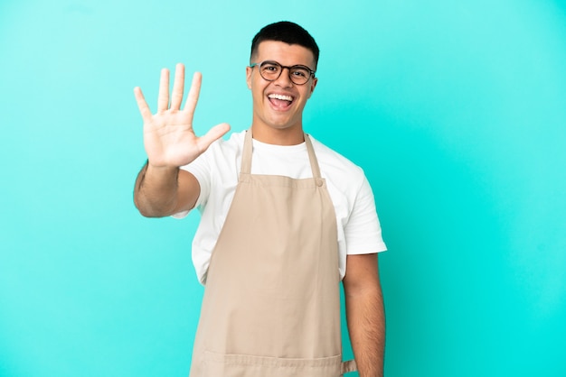 Restaurant waiter man over isolated blue background counting five with fingers