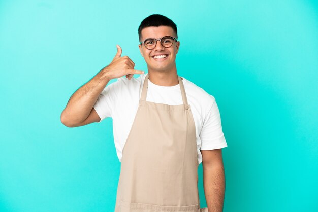 Restaurant waiter man over isolated blue background making phone gesture. Call me back sign