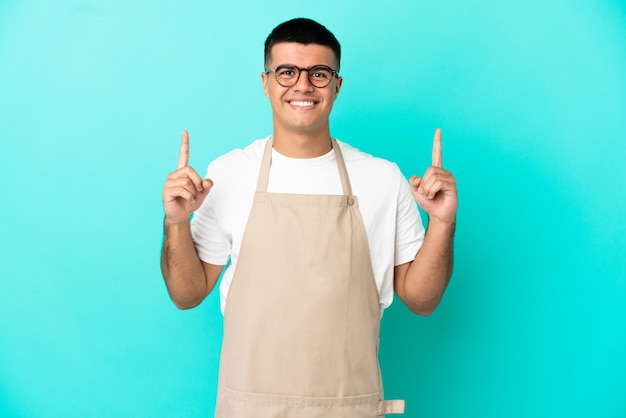 Restaurant waiter man over isolated blue wall pointing up a great idea