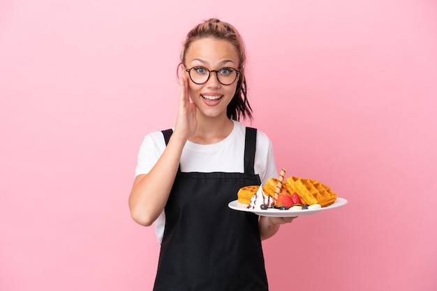 Restaurant waiter Russian girl holding waffles isolated on pink background with surprise and shocked facial expression