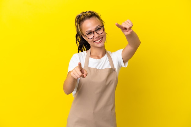 Restaurant waiter Russian girl isolated on yellow background points finger at you while smiling