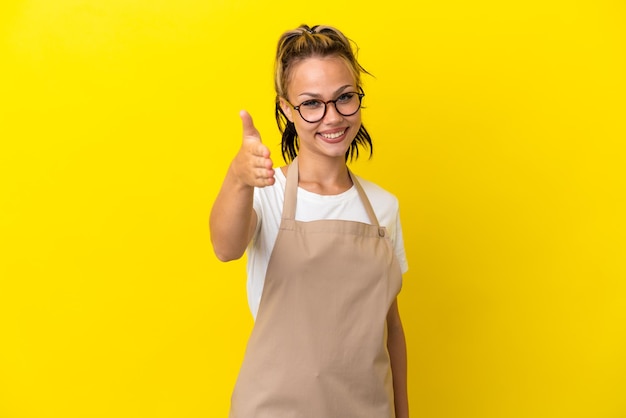 Restaurant waiter Russian girl isolated on yellow background shaking hands for closing a good deal