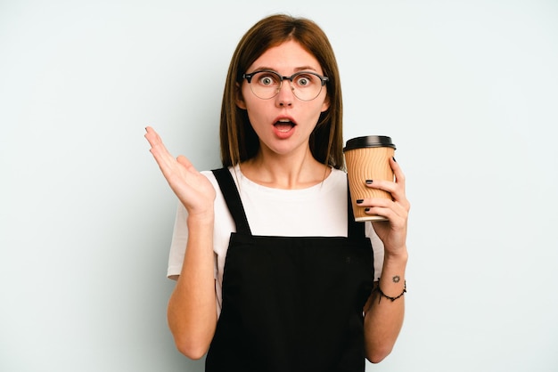 Restaurant waiter woman holding a take away coffee isolated on blue background surprised and shocked.