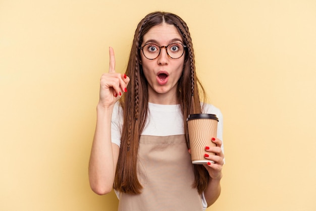 Restaurant waiter woman holding a take away coffee isolated on yellow background having an idea, inspiration concept.