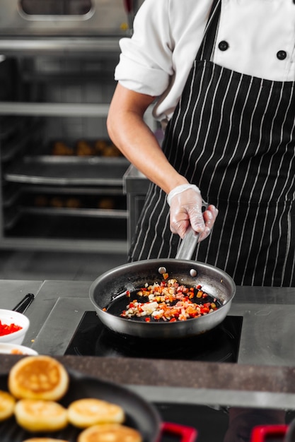 Restaurantchef-kok die italiaanse mirepoix kookt die in een pan op de keuken sauteert