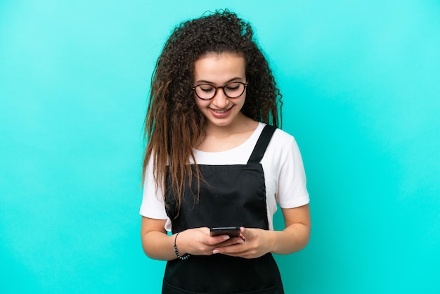 Restaurantkelner Arabische vrouw die op blauwe achtergrond wordt geïsoleerd die een bericht met mobiel verzendt