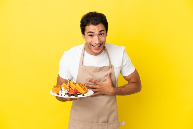 Restaurantkelner met wafels over geïsoleerde gele achtergrond die veel lacht