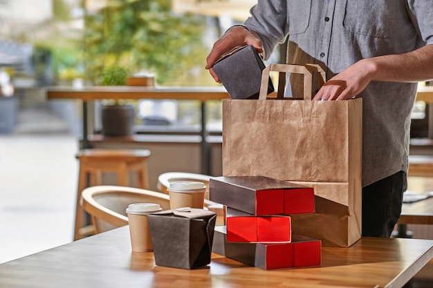 Restaurantmedewerker die voedseldozen inpakt om mee te nemen. stelletje lege wegwerpcontainers voor afhaalmaaltijden gestapeld met papieren zakken en dozen met kopieerruimte voor het merklogo.