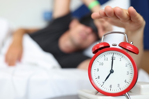 Rested man reaches for watch button to turn off daily alarm and wake up wake up time concept