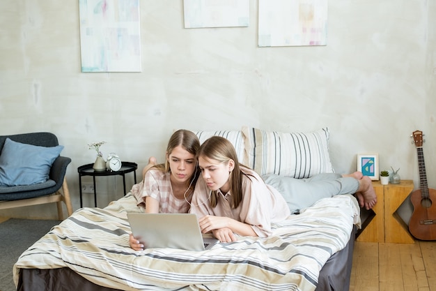 Restful teenage twins in earphones watching online movie